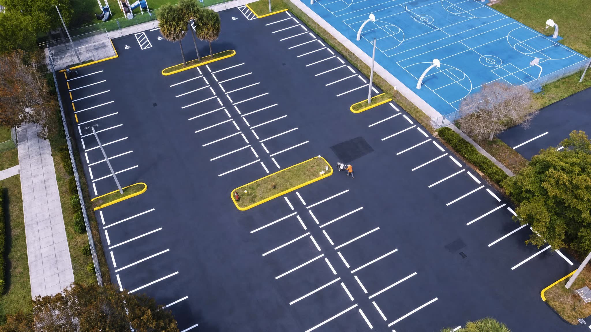 School parking lot and blue basketball courts beside freshly striped black asphalt