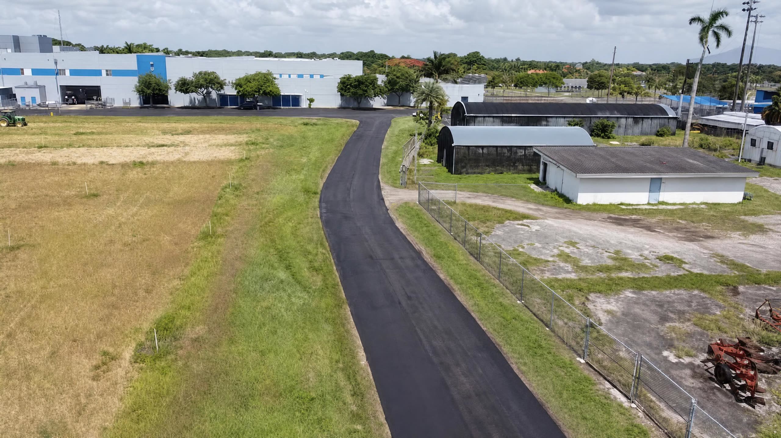 The same access road finished in fresh black asphalt, curving toward the facility