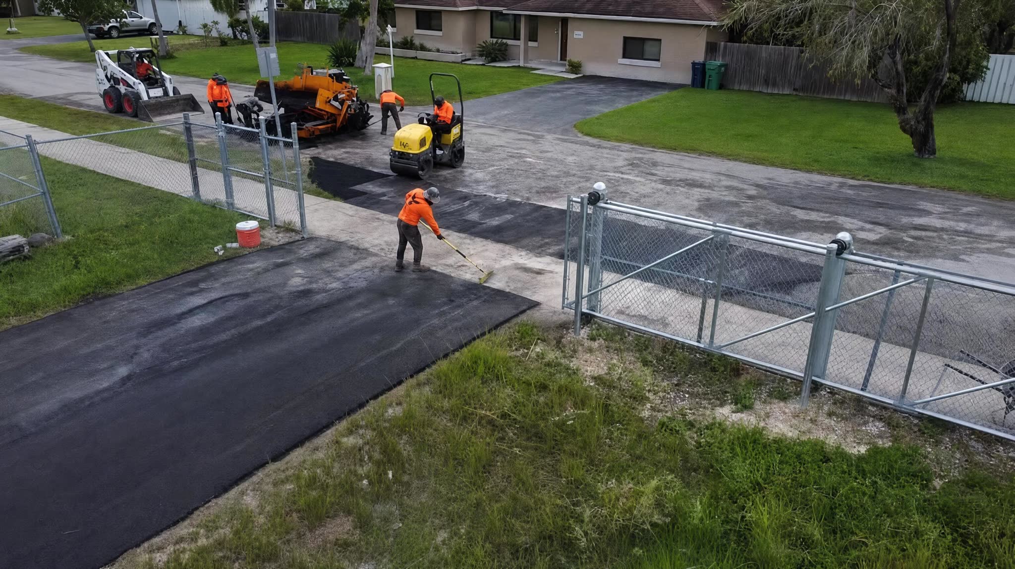 Phoenix crew in orange hi-vis compacting a fresh asphalt driveway apron with a roller
